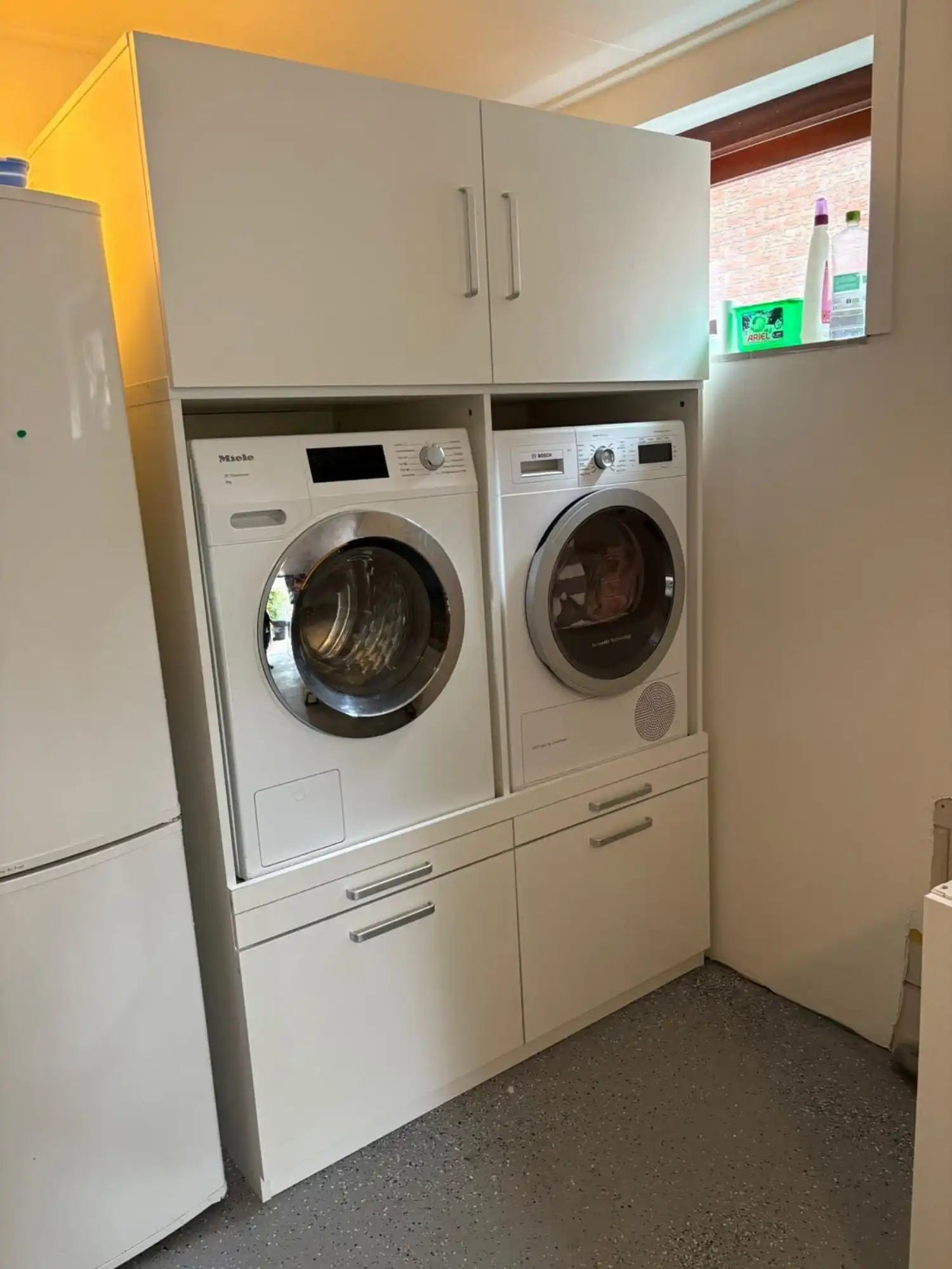Een witte gestapelde wasmachine en droger met hangkasten bovenop.