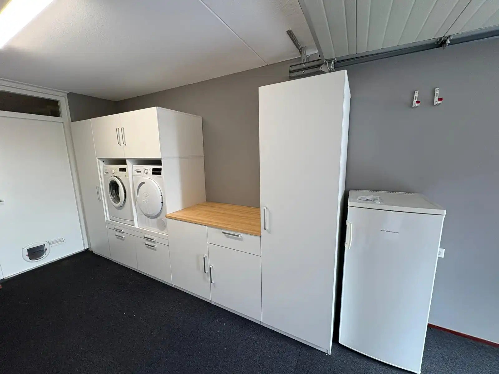 Een wit wasruimte kastensysteem met geïntegreerde wasmachine, droger en een hoog vriesunit.